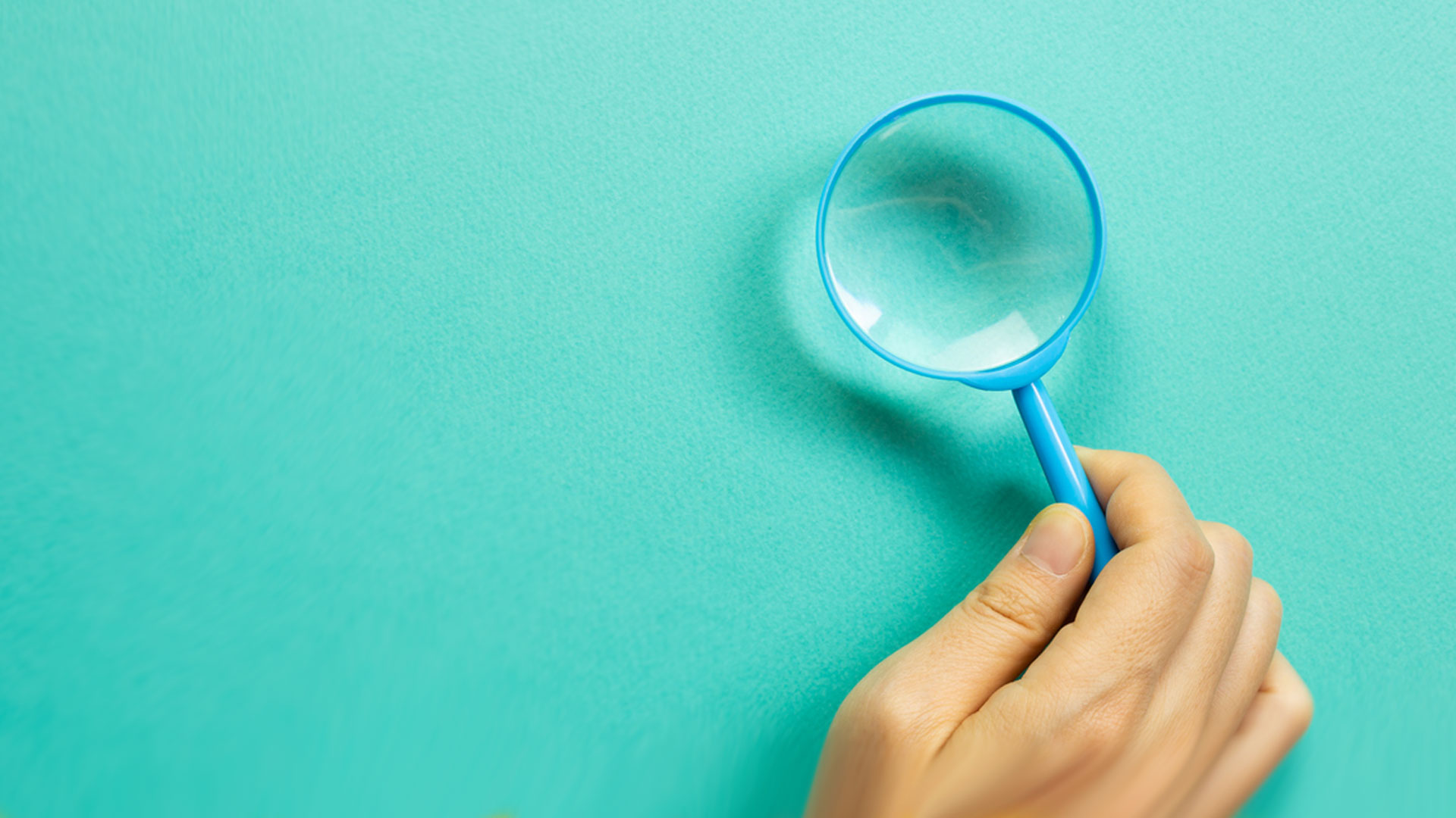 Hand holding a blue magnifying glass on green background. top view