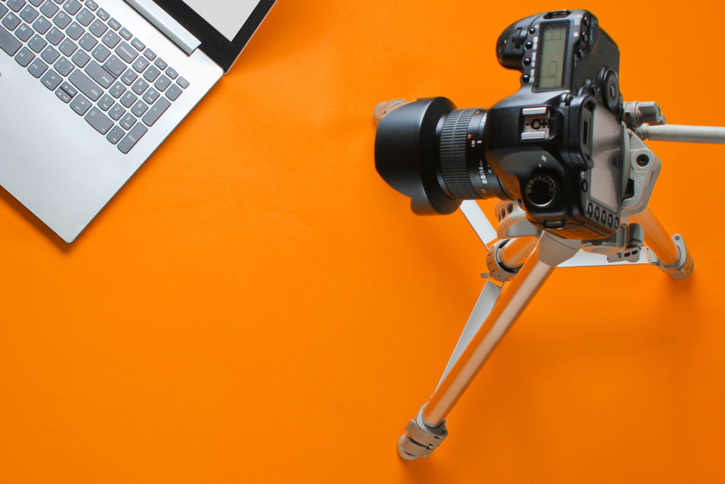 Camera on tripod, laptop on orange background.