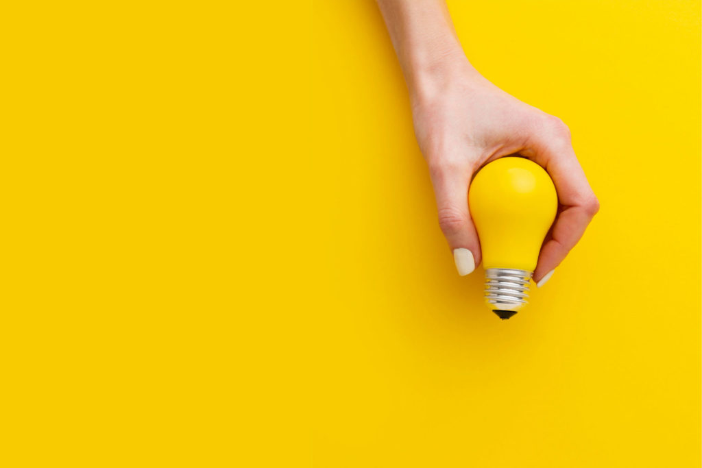 hand holding yellow lightbulb against yellow background