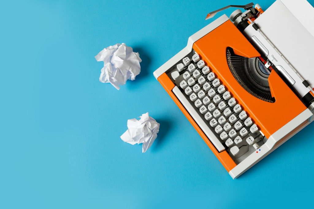 orange typewriter and crumpled paper on bright blue background naming project aventi