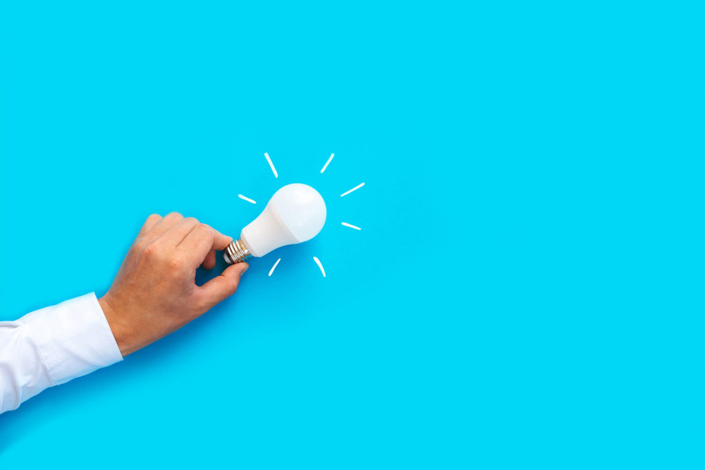 blue background hand holding lightbulb for rethinking innovation