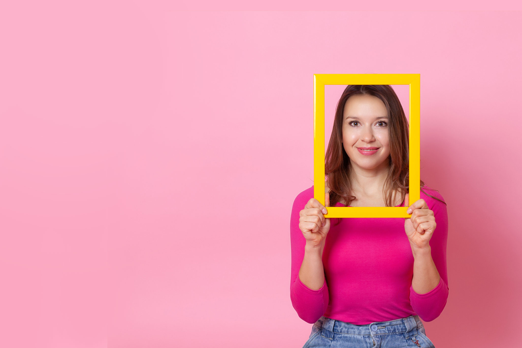 close-up portrait of a young woman with a face inside an empty yellow frame, that she holds in her hands, isolated on a pink background - for buyer personas.