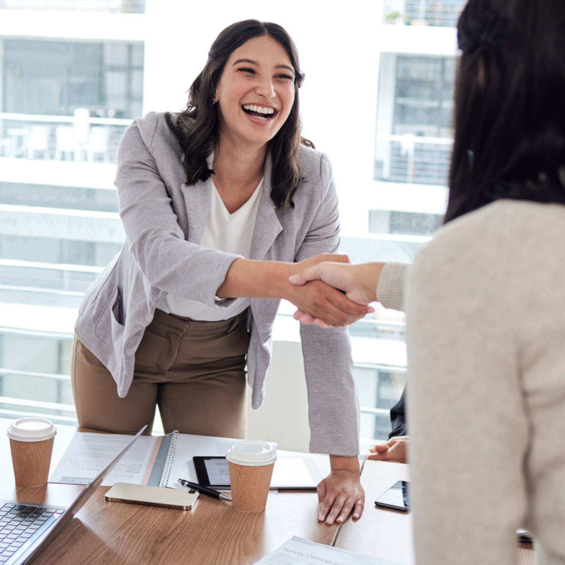 A professional smiling and shaking hands across a desk, representing Aventi Group’s credible third-party perspective that aligns teams and reduces internal debate.