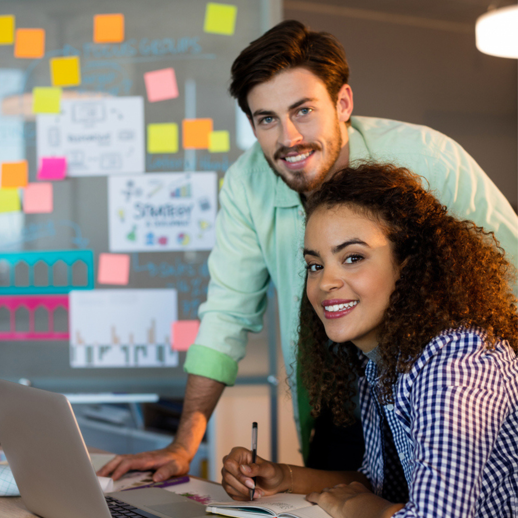 Two marketers collaborating at a laptop in a workspace with sticky notes and charts, highlighting Aventi Group as a specialized B2B SaaS product marketing agency.